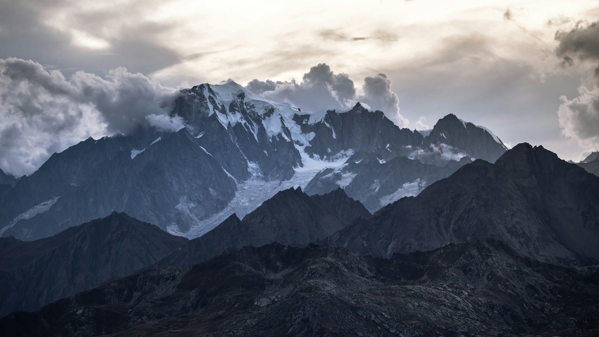The snow-covered Mont Blanc massif under heavy cloud, above darker foreground ridges